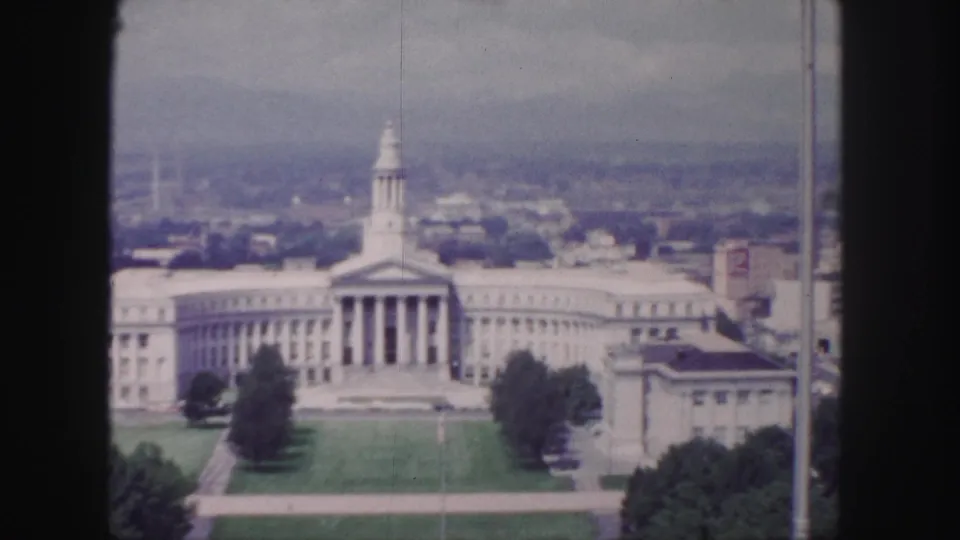 1958 Denver frame showing the columned building from above, with the lawn and flanking trees softened by 8mm grain and haze.