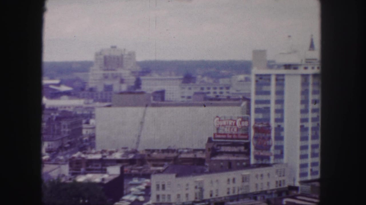 1958 Denver skyline view with a construction crane, rooftop structures, a Country Club Beer billboard, and a tall modern building at right.