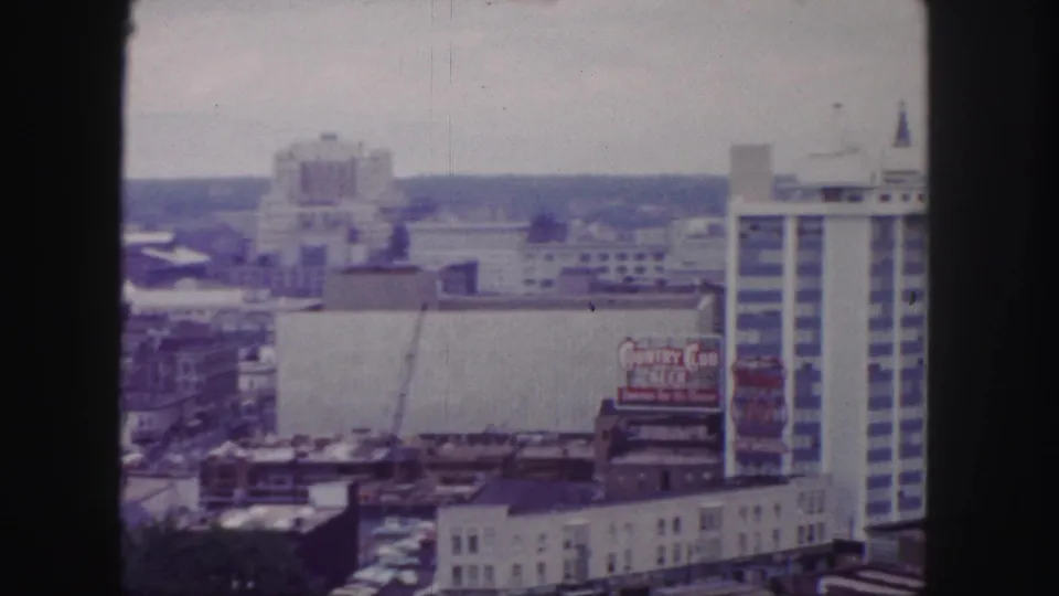 1958 Denver skyline view with a construction crane, rooftop structures, a Country Club Beer billboard, and a tall modern building at right.