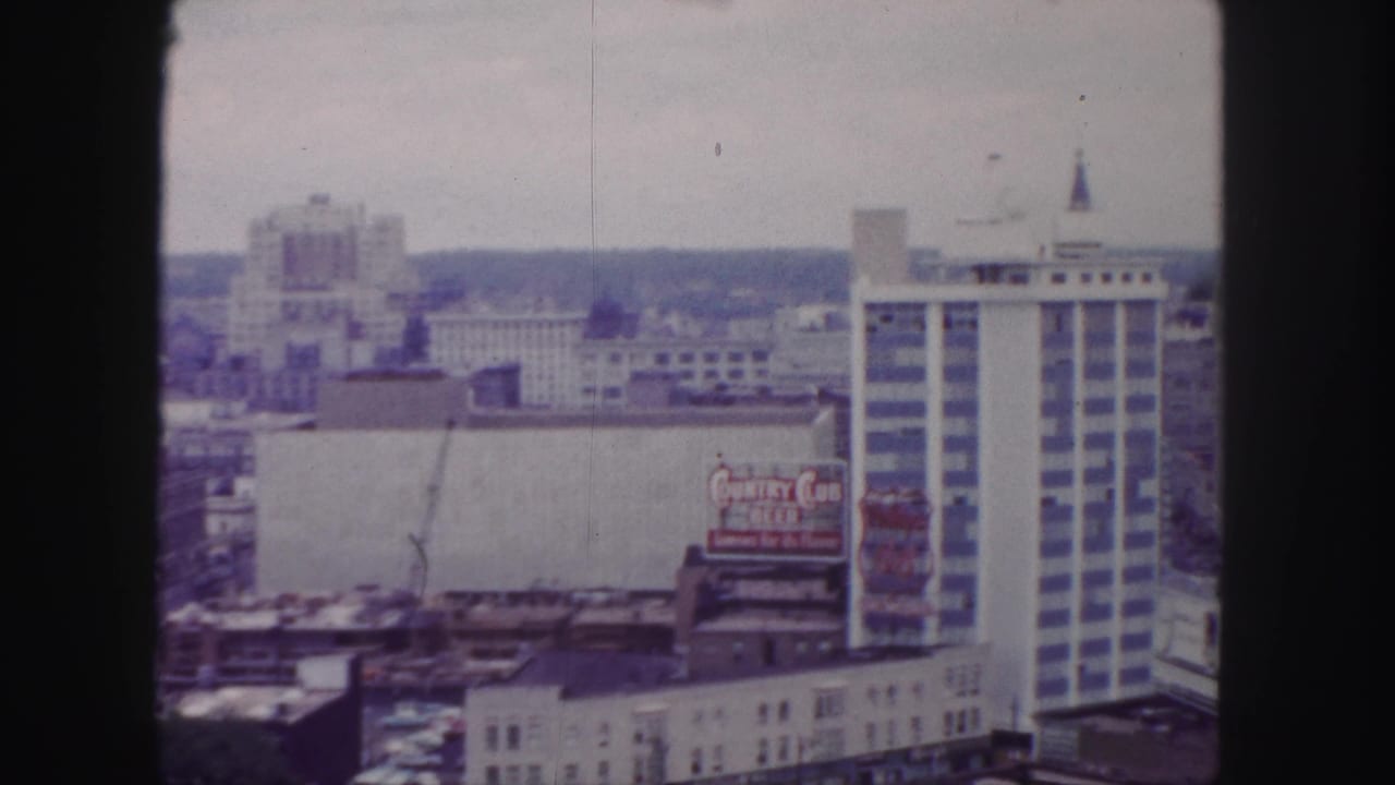 1958 Denver cityscape with a visible Country Club Beer billboard, pale construction wall, crane, and tall building with vertical window bands.
