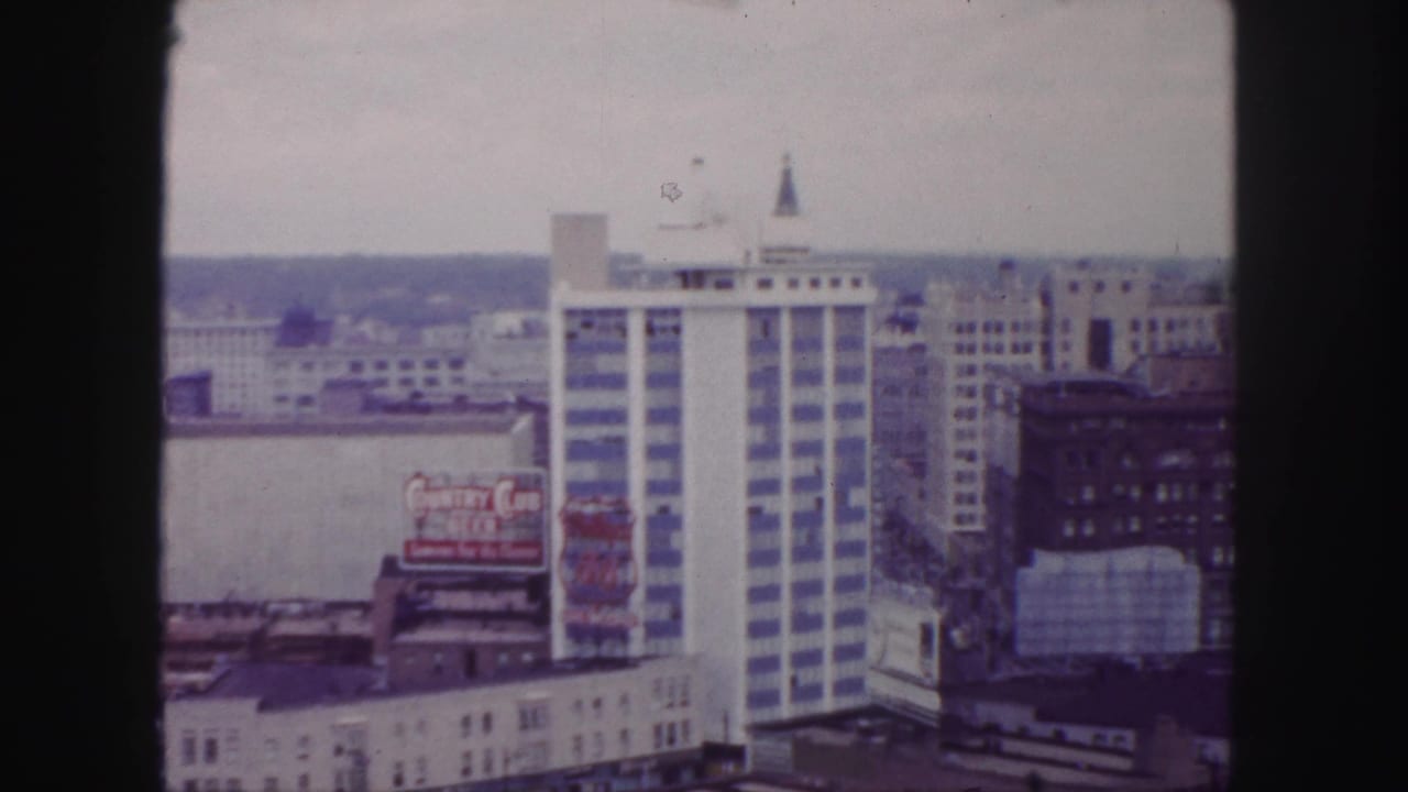 Downtown skyline with a white striped high-rise, rooftop billboard, and dark film borders.