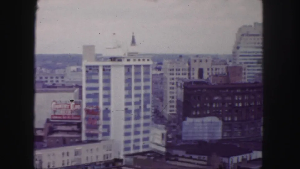 1958 Denver downtown view with rooftop signage at left, a striped high-rise near center, and taller buildings entering at right.