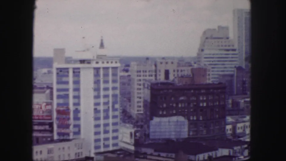 1958 Denver downtown skyline with a white striped high-rise, darker brick buildings, rooftop billboard, and distant urban horizon.