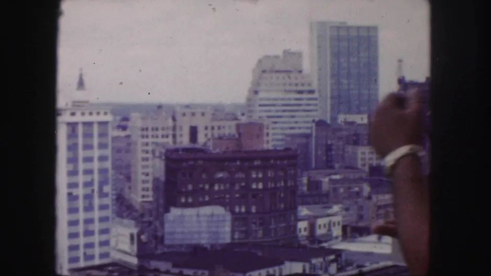 Denver skyline view with the home-movie operator's hand or arm briefly intruding near the right edge of the frame.