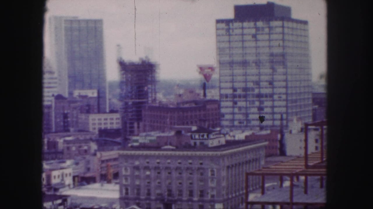 1958 Denver high-angle skyline view with tall buildings, a construction site, rooftop lettering, and a red-yellow triangular sign.