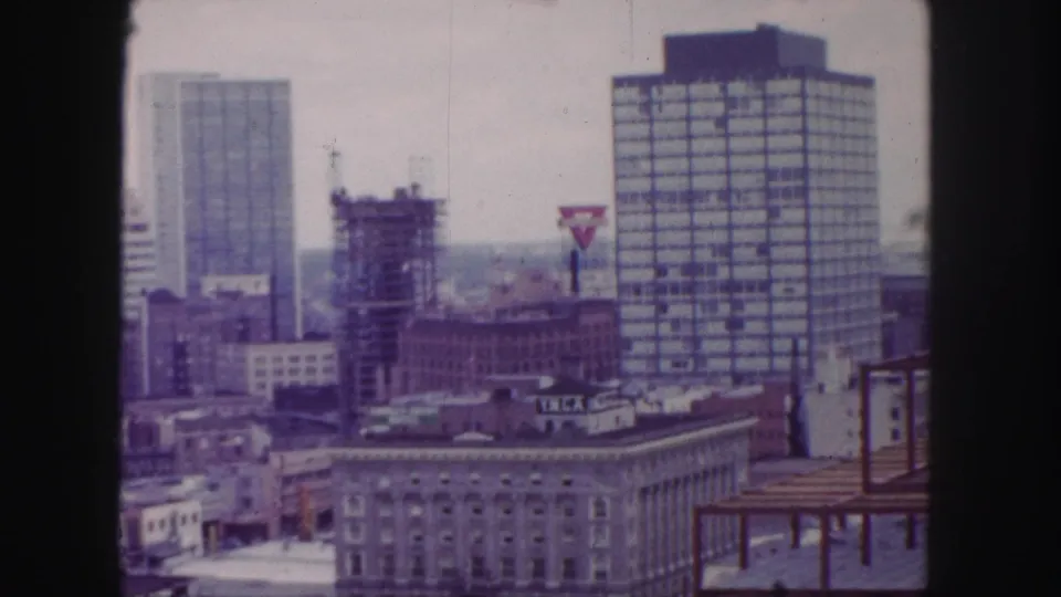 1958 Denver skyline view with a tall glassy building, construction site, commercial signage, and foreground rooftops.
