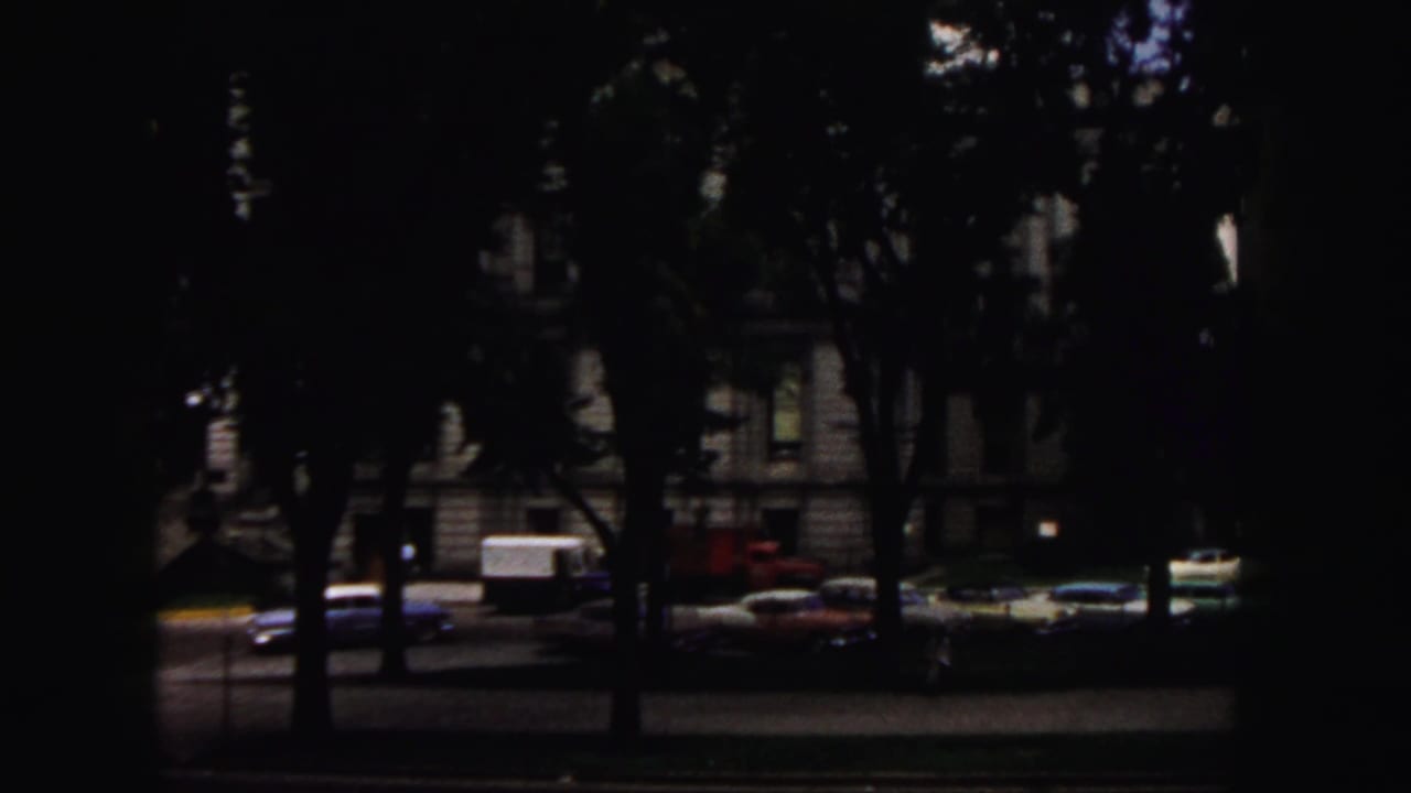 Tree-shaded Denver street scene with parked period cars and a masonry building visible through dark exposure.