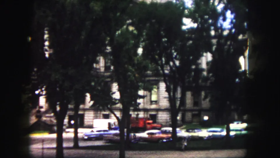 1958 Denver street view with mature trees, parked classic cars, a white vehicle, and older building facades.