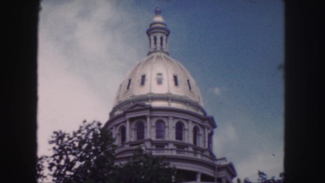 Closer view of a domed capitol roof and lantern against blue sky and clouds.