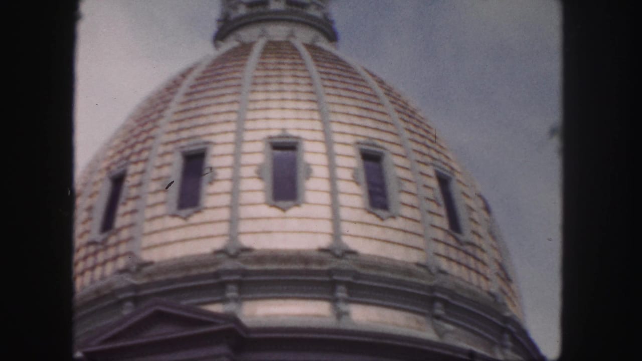 Ornate dome seen from below with tiled roof, windows, and cloudy sky.