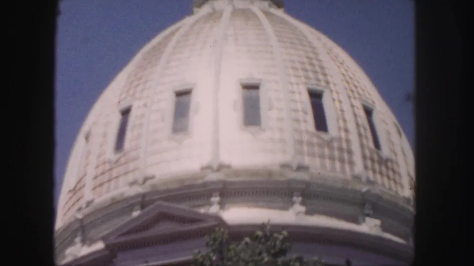 1958 Denver 8mm frame showing the lower curve of an ornate tiled dome with narrow windows and tree branches below.