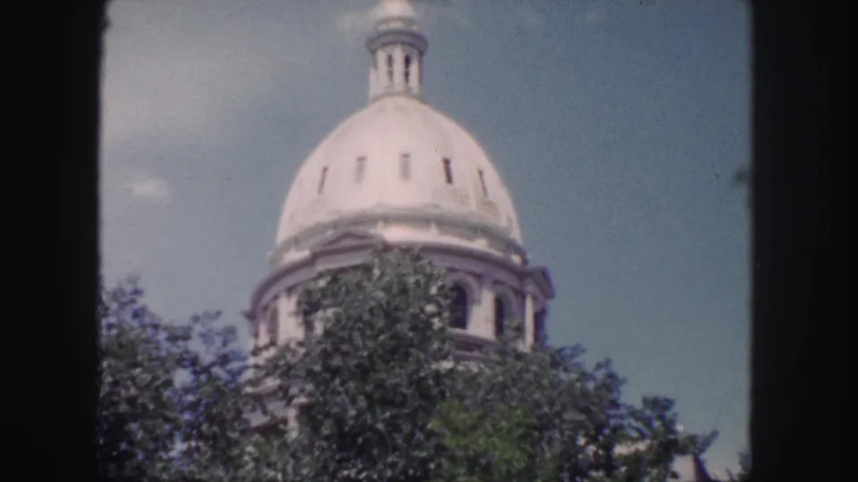 1958 Denver home-movie frame showing the domed historic building partially obscured by trees beneath a pale blue sky.