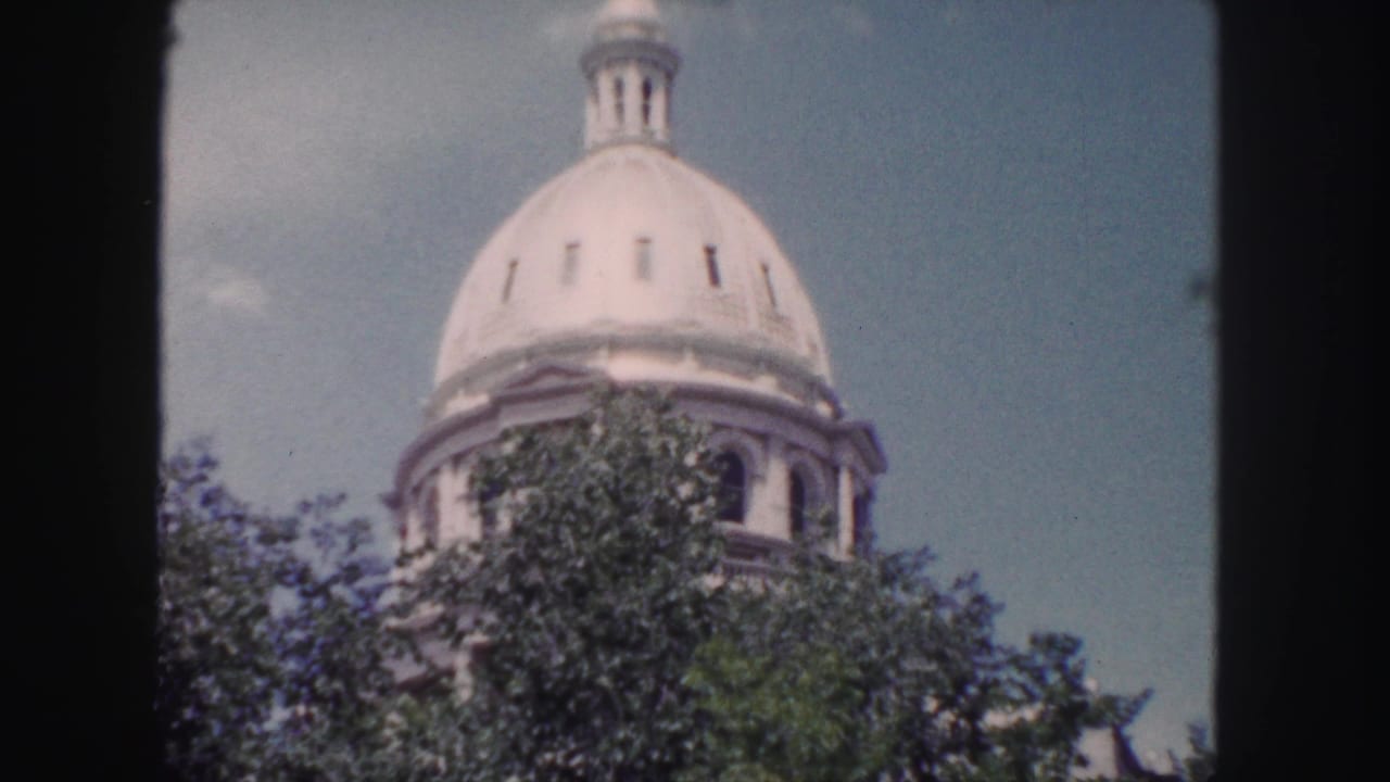 1958 Denver home-movie view of the Colorado State Capitol dome partly obscured by trees.