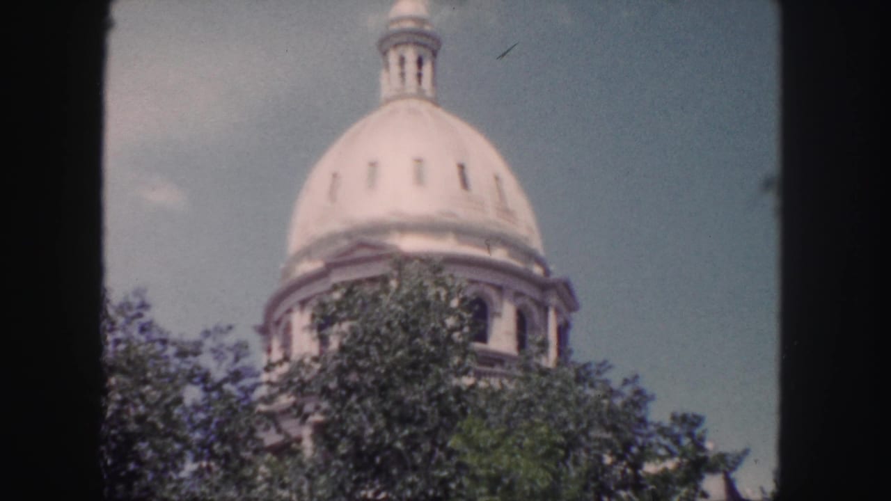 The Colorado State Capitol dome appears above treetops in a soft, grainy 1958 Denver 8mm frame.