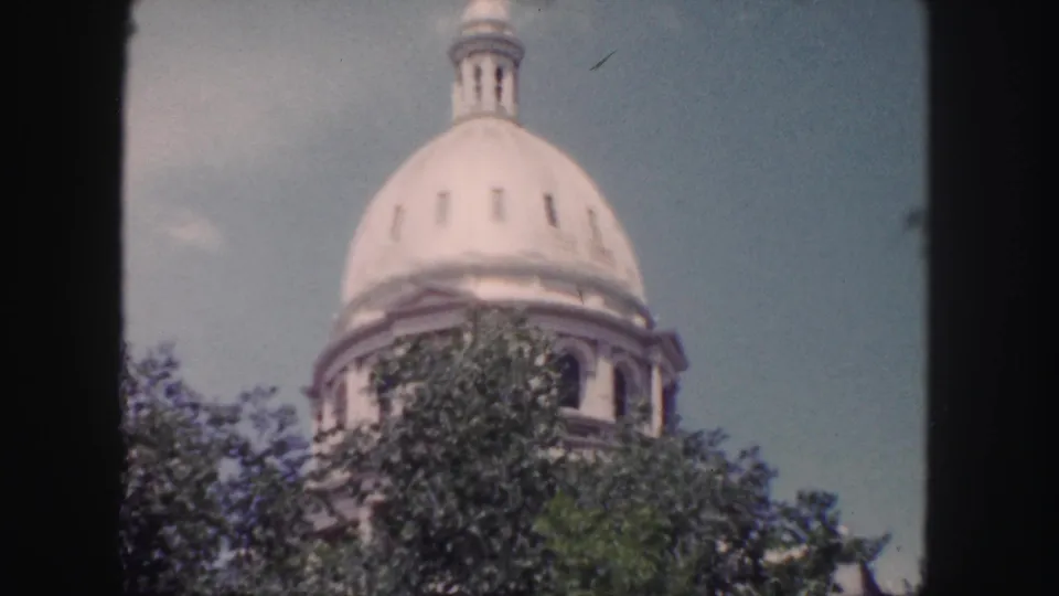 The Colorado State Capitol dome appears above treetops in a soft, grainy 1958 Denver 8mm frame.