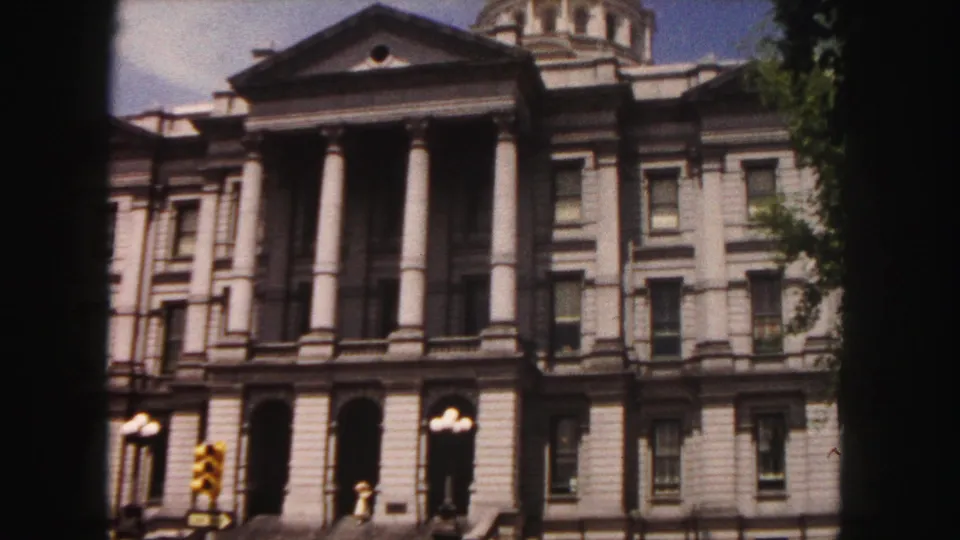 1958 Denver home-movie frame showing the Colorado State Capitol facade, columns, partial golden dome, streetlights, and traffic signal.