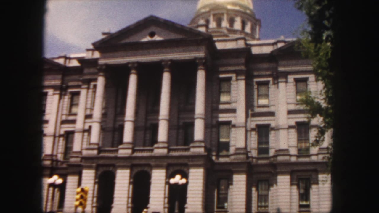 Capitol building front with columns, arched doors, streetlights, and partial dome.