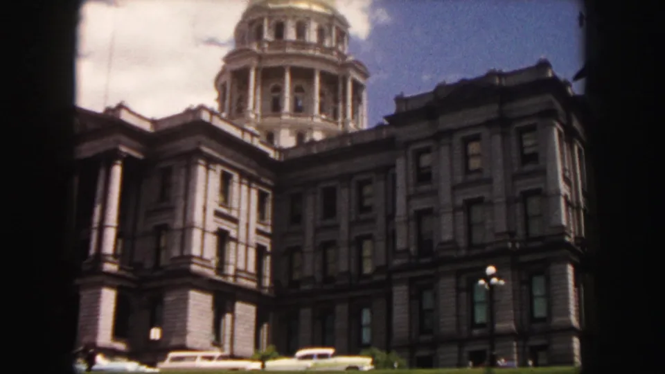 1958 Denver frame showing an angled view of the Colorado State Capitol dome, side facade, streetlights, and cars along the street.