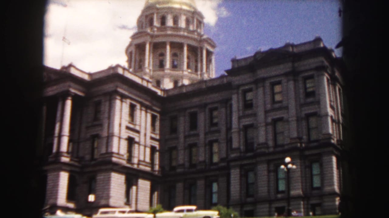Colorado State Capitol exterior with dome, stone facade, street lamp, sky, and parked cars.