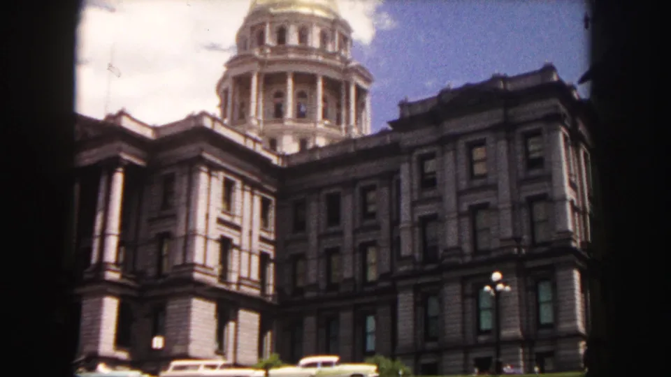 1958 Denver home-movie frame showing the Colorado State Capitol dome above the stone facade, with a street lamp and parked cars below.