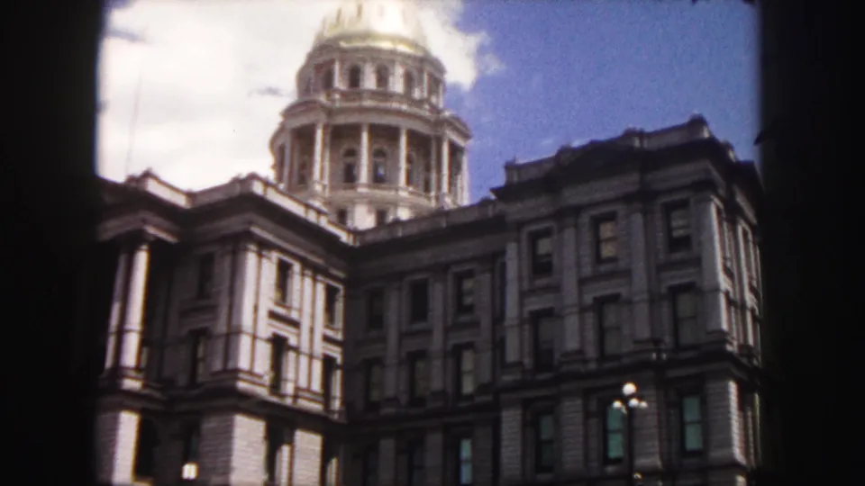 1958 Denver frame showing a closer handheld view of the Colorado State Capitol dome, upper facade, windows, clouds, and street lamp.