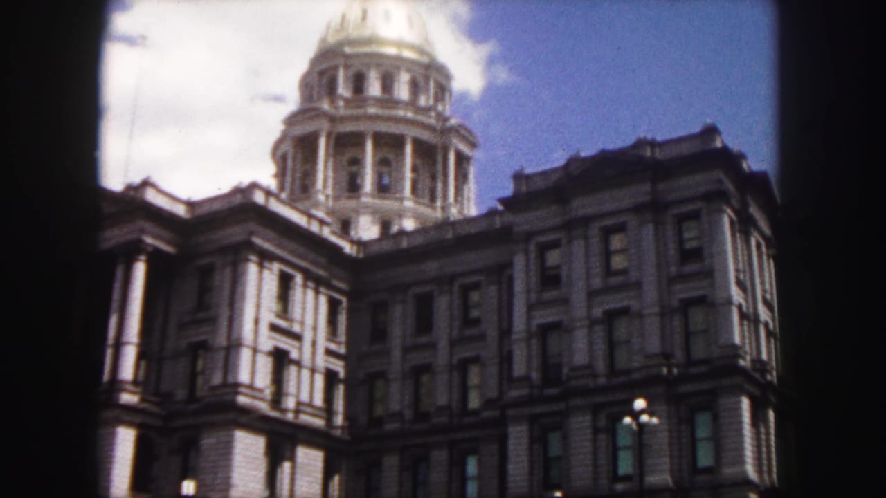 1958 Denver home-movie frame showing the Colorado State Capitol stone facade and golden dome from a low visitor viewpoint.