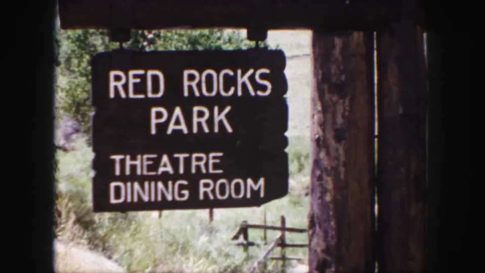Visitor-shot 8mm frame of the Red Rocks Park sign, with theatre and dining room text visible on a wooden wayfinding board.
