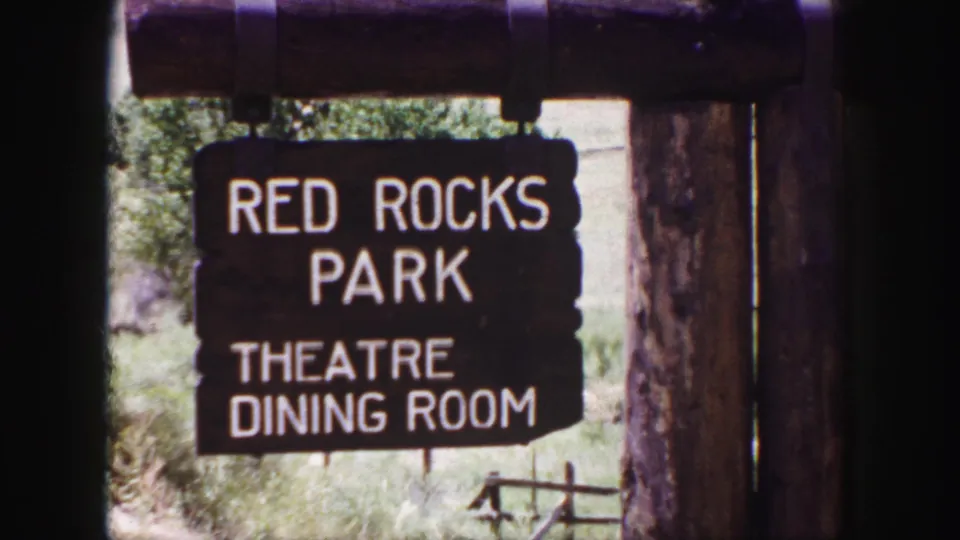 Close 1958 home-movie view of a dark wooden Red Rocks Park sign with white lettering for the theatre and dining room.