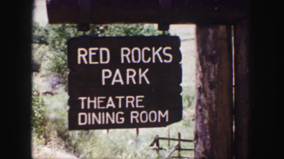 1958 8mm close-up of the Red Rocks Park sign, with timber framing and bright brush visible around the lettering.