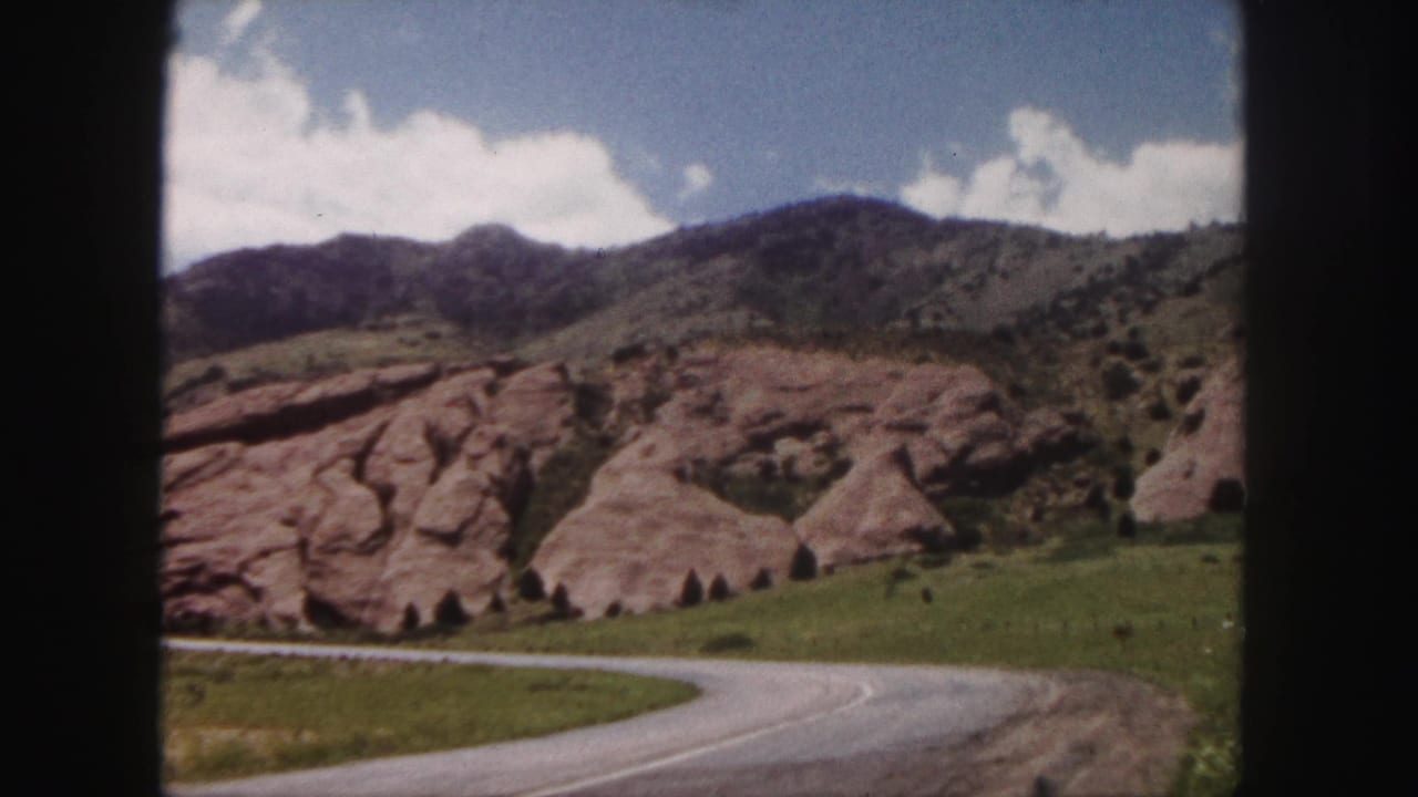 Denver-area red rock landscape with a curving road, grassy slope, and mountain ridge in 1958 home-movie footage.
