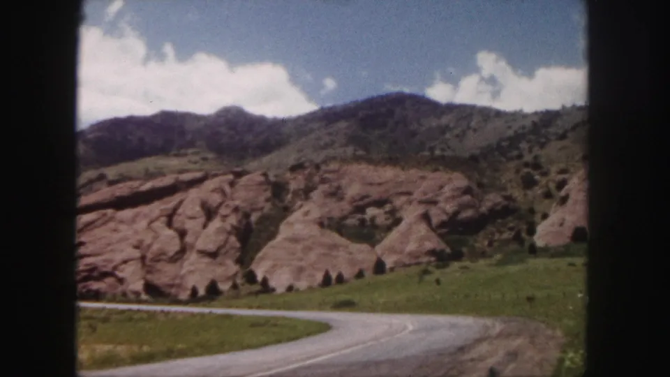 Denver-area red rock landscape with a curving road, grassy slope, and mountain ridge in 1958 home-movie footage.