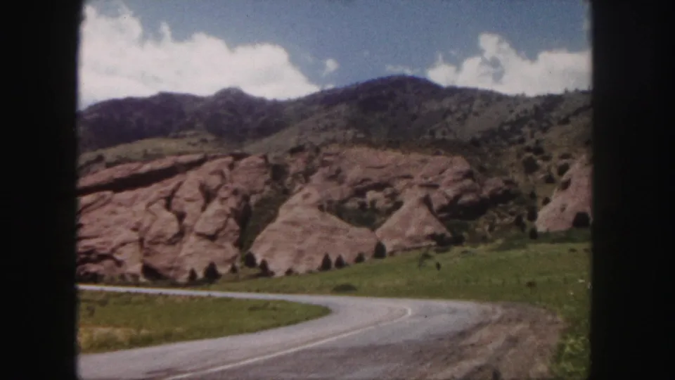 Final 1958 frame of a Denver-area winding road below red rock formations and a grassy mountain ridge.