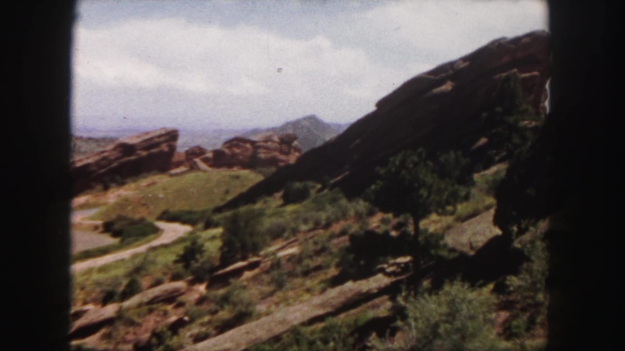 1958 8mm view of Red Rocks near Denver, showing sandstone outcrops, a curving path, scrub vegetation, and distant mountain shapes.