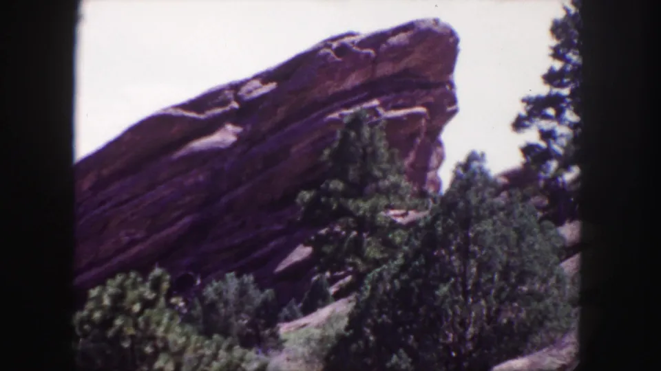 1958 8mm Red Rocks view near Denver, showing an angled sandstone formation above evergreen trees with visible grain and color shift.