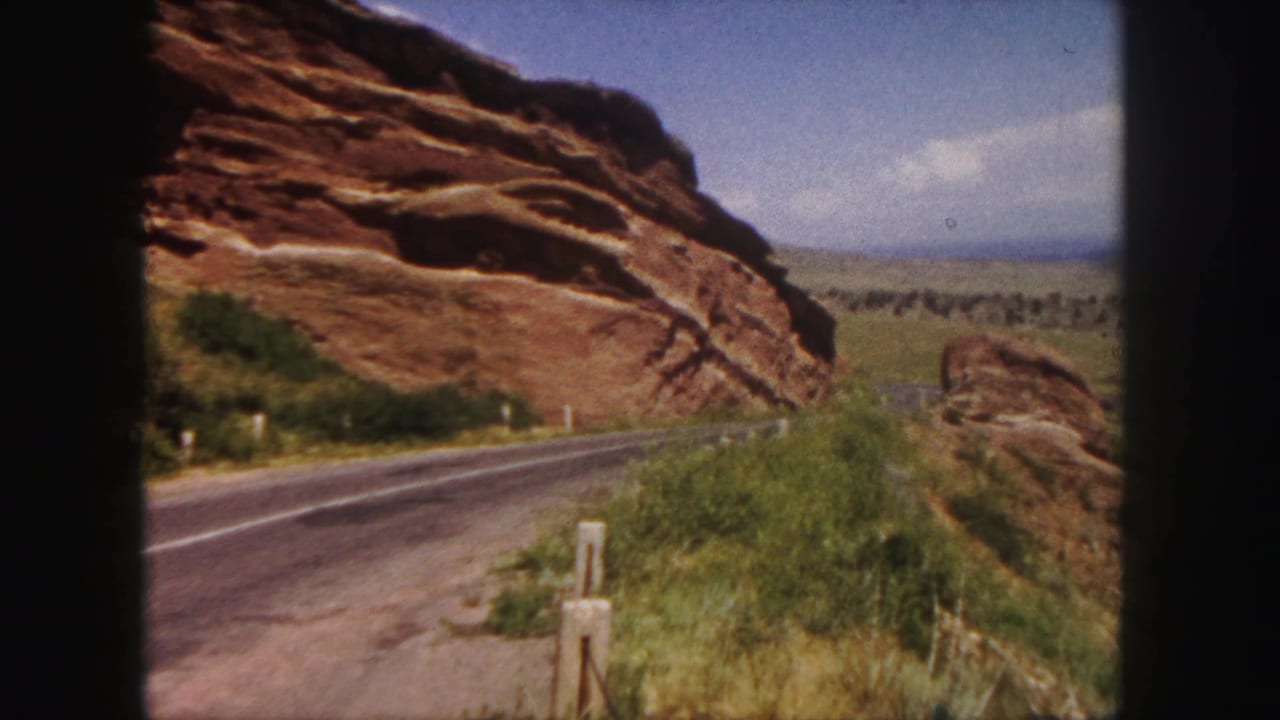 Two-lane road beside large red rock formations and roadside grass.