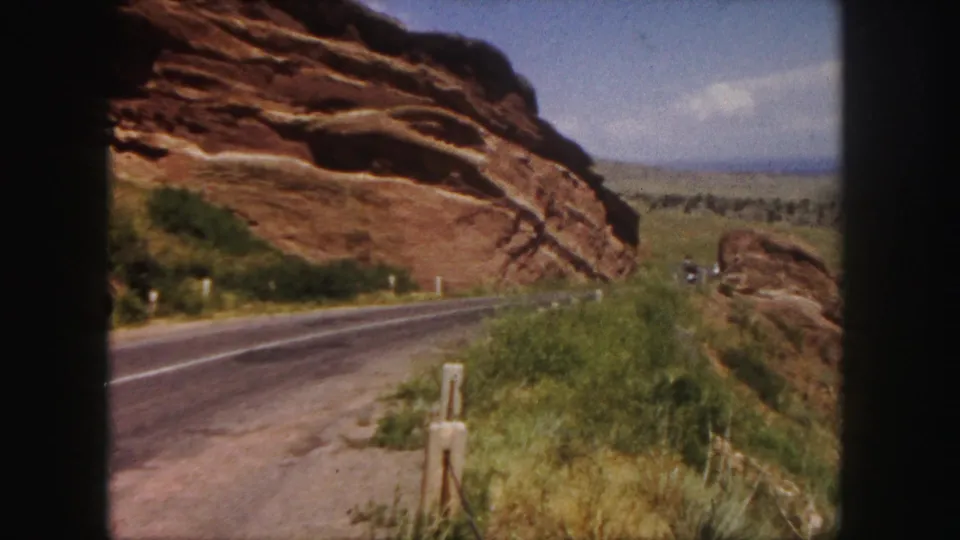 The final frame holds on the road, red rock cliff, grass, and small distant vehicles in the Denver-area landscape.