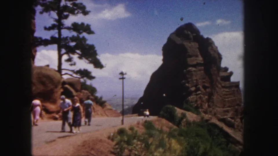 Visitors stand and walk near a red rock roadside in the 1958 Denver-area home movie footage.