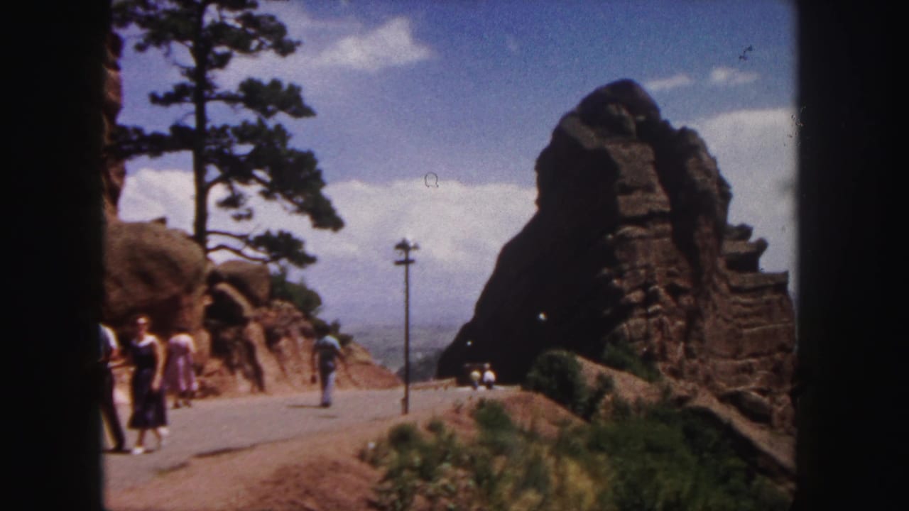 Small groups of people walking near red rock formations on a paved overlook road.