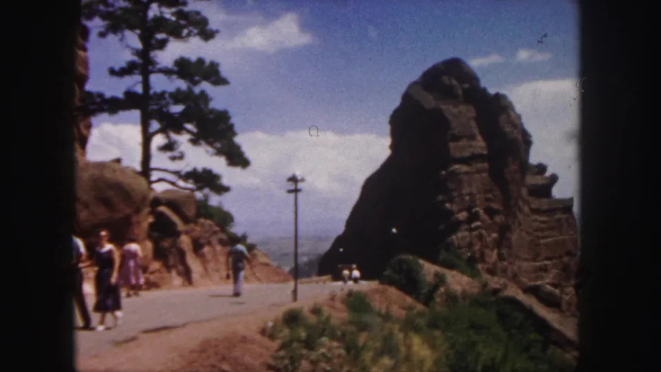 Visitors in period clothing move along a paved road near red rock formations in the supplied 1958 Denver, Colorado clip.