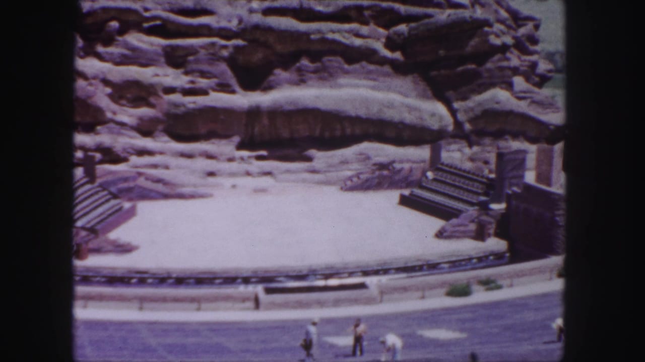 A circular outdoor stage area sits below rock formations with visitors in front.