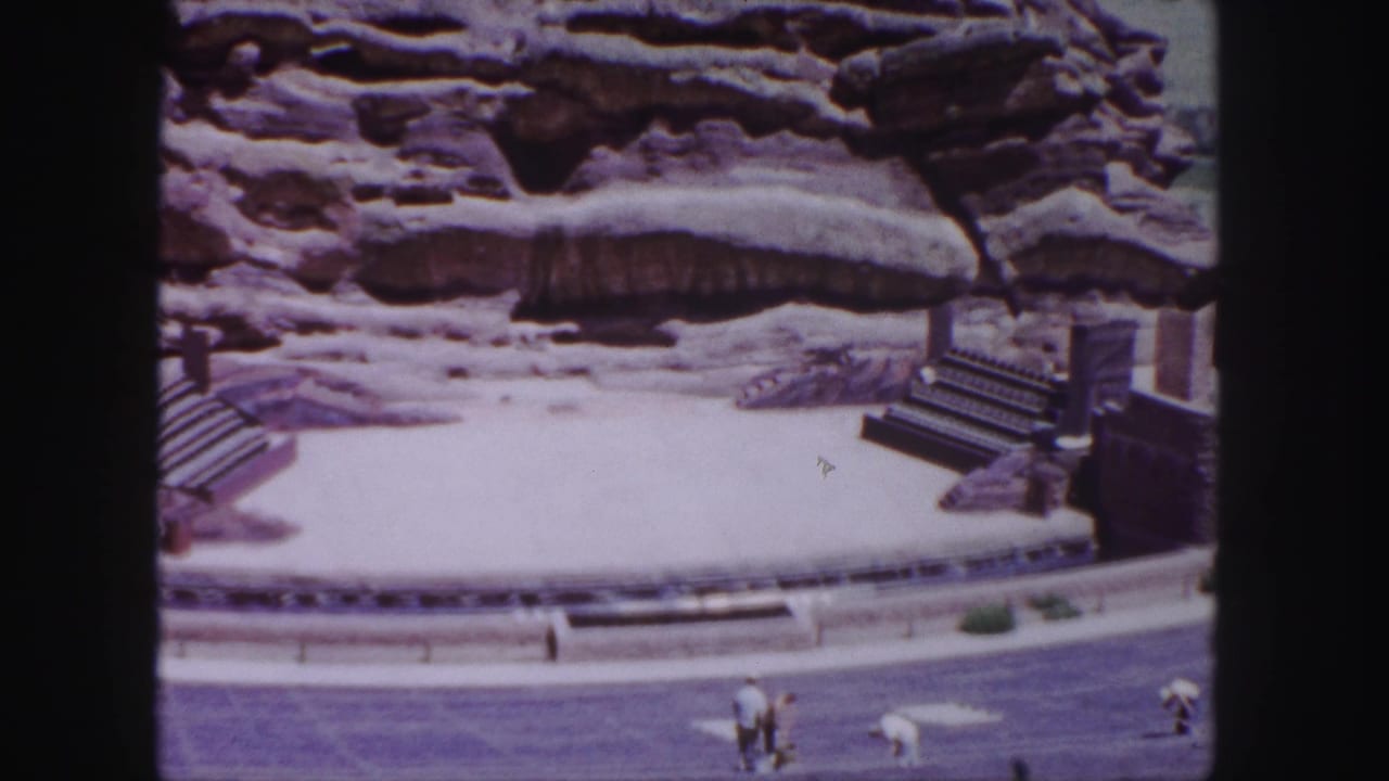 Red Rocks Amphitheatre stage with sandstone backdrop and small visitors below.