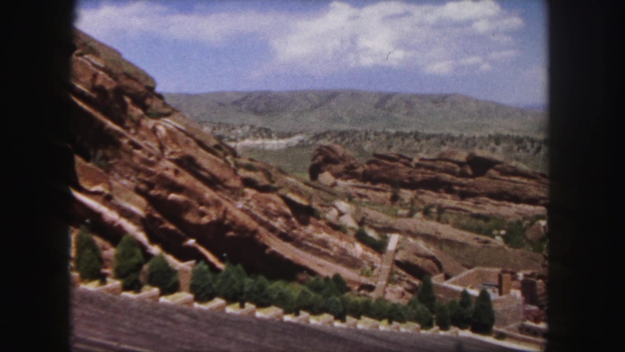 Red rock slope and distant hills under a partly cloudy sky.