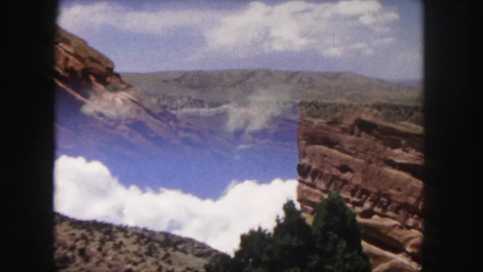 A shifted 1958 8mm Colorado frame catches blue sky, white clouds, a red rock wall, brush, and distant hills.