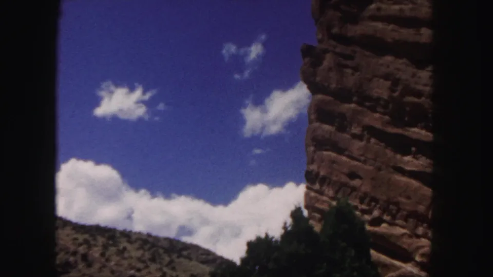 Denver-area mountain scenery on 8mm film, with red rock at right, a scrub hillside, clouds, and dark foreground edges.
