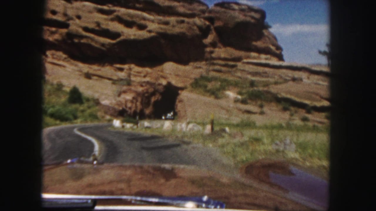 1958 8mm car-view footage near Denver shows a winding two-lane road approaching red rock walls and a tunnel area.