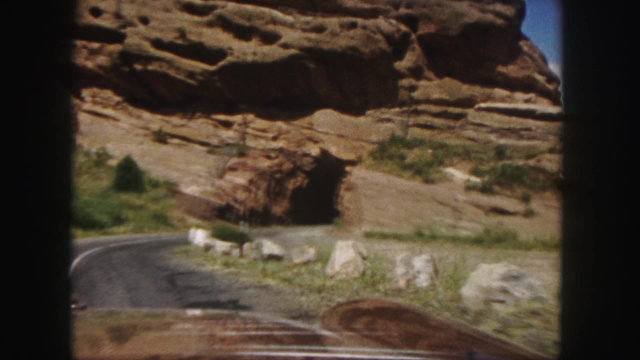 Dashboard view of a road curving toward a red rock tunnel opening.