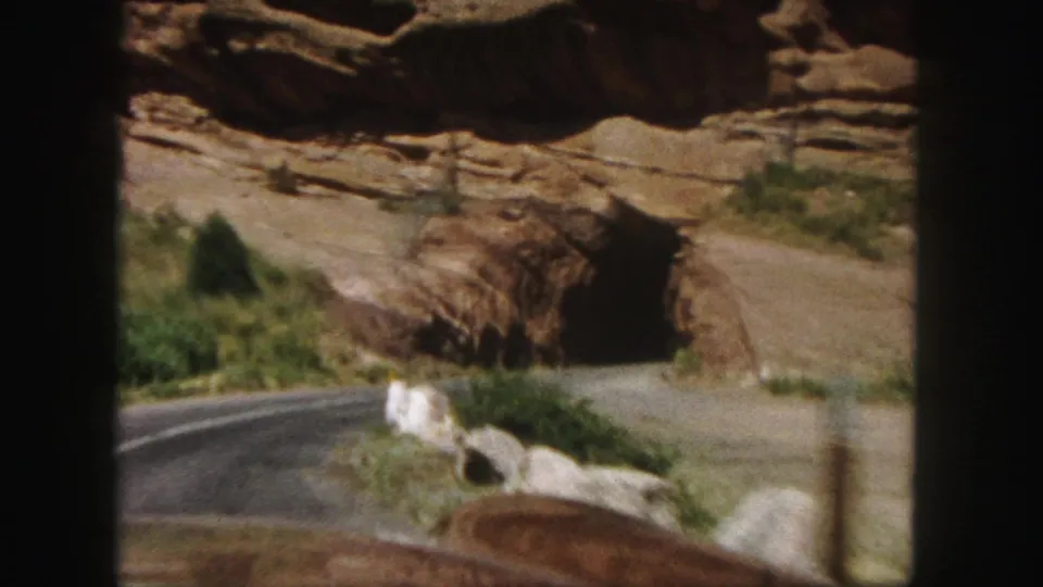 The 8mm frame shows a close car-view approach to a red rock tunnel entrance along a narrow Colorado road.
