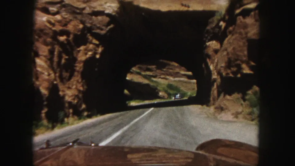 From inside the car, the road leads into a shadowed red rock tunnel, with the vehicle hood visible at the bottom of the frame.