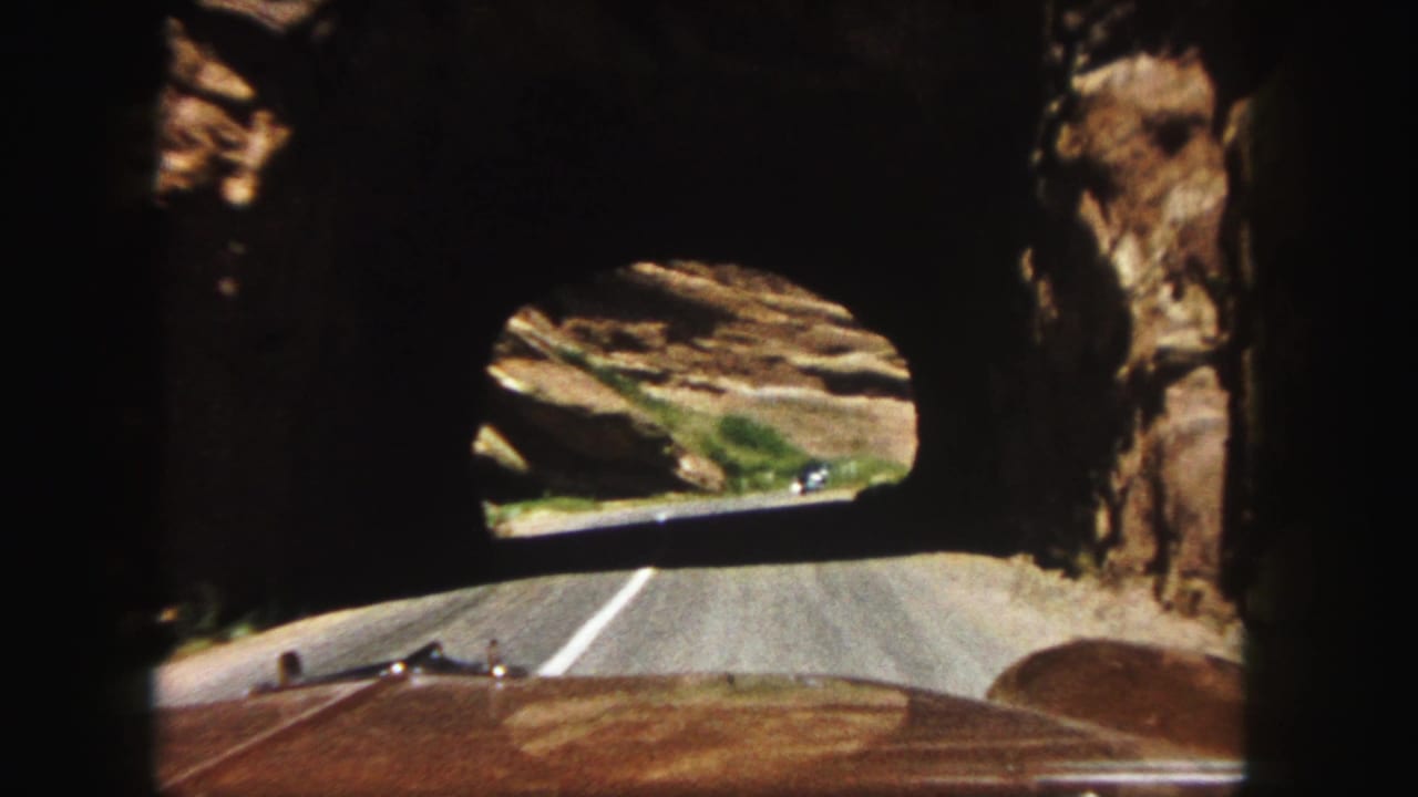 1958 8mm road-trip view from inside a car driving through a rock tunnel toward a sunlit two-lane road.