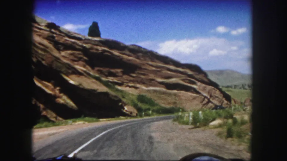 1958 home-movie view of a paved road running alongside layered red rock formations in Colorado terrain.
